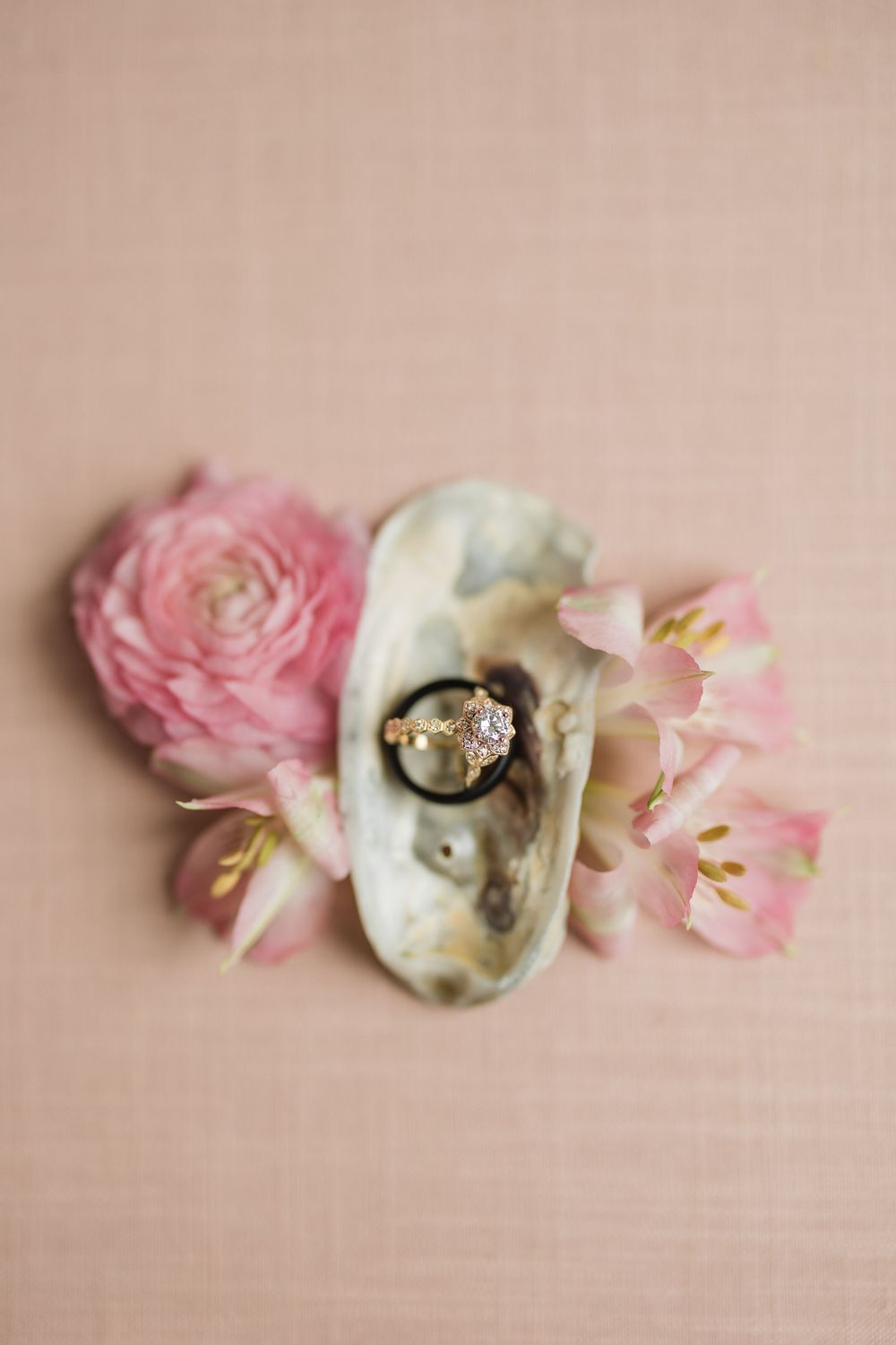 A delicate arrangement of pink ranunculus flowers and vintage lace fabric laid out on a beige textured background.