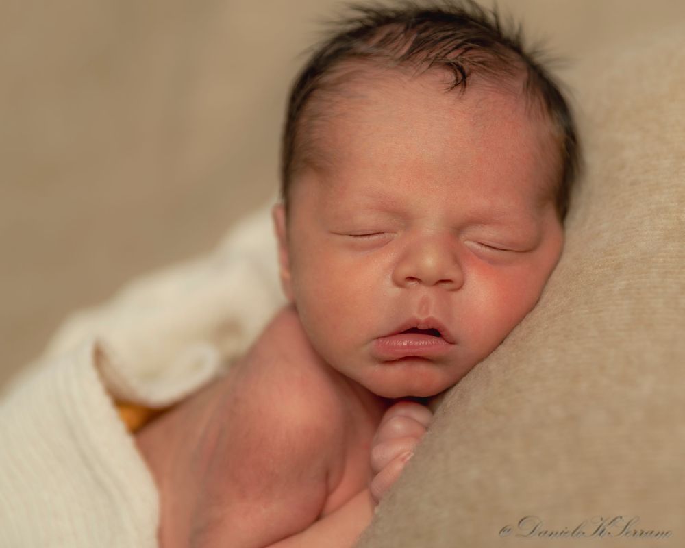 Peaceful newborn baby sleeping with dark hair, wrapped in white cloth, professional newborn photography.