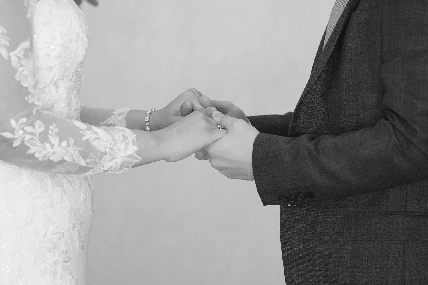 A black and white photograph showing hands exchanging rings during a wedding ceremony.