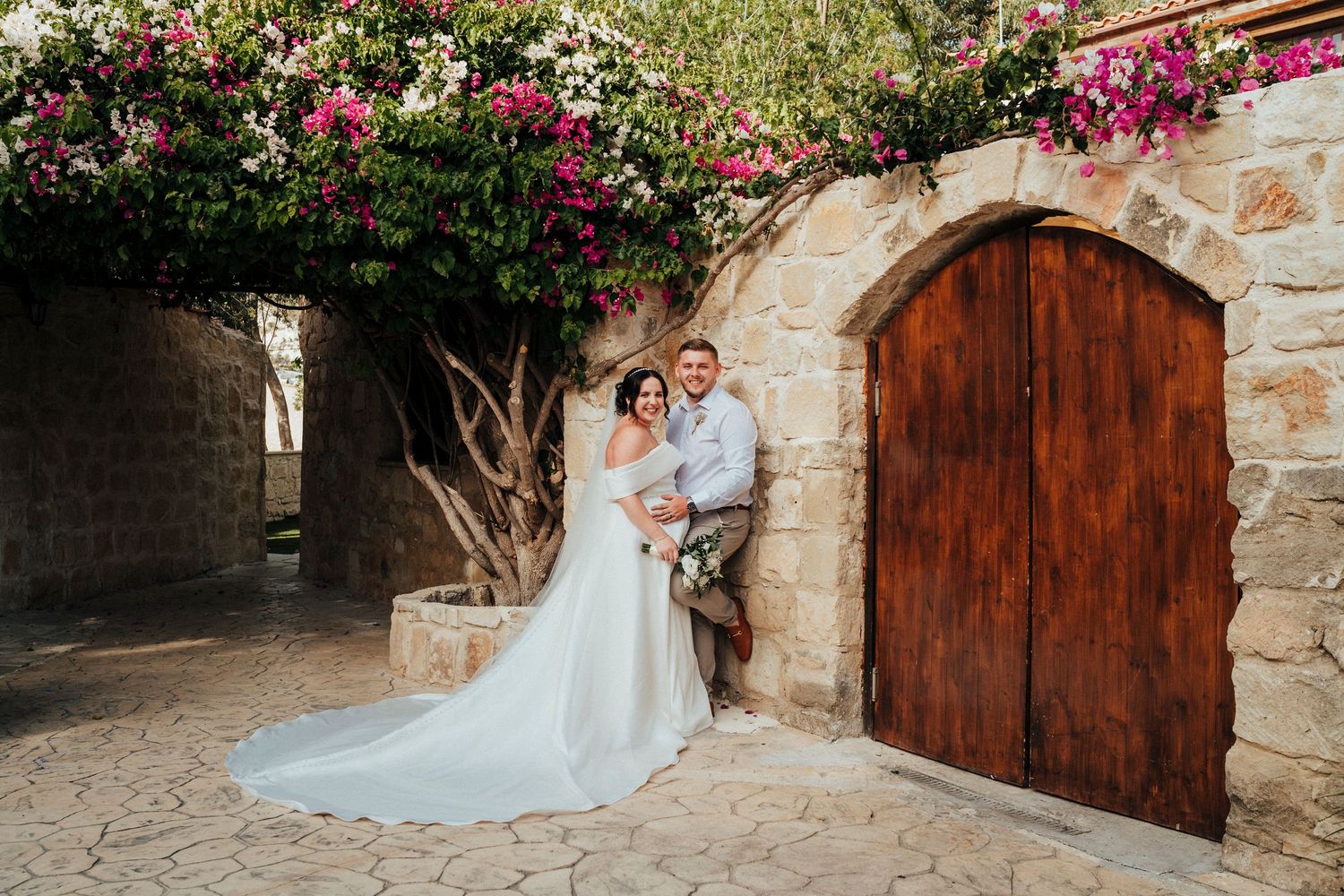 A romantic wedding moment captured among lush greenery with two people embracing in formal attire.