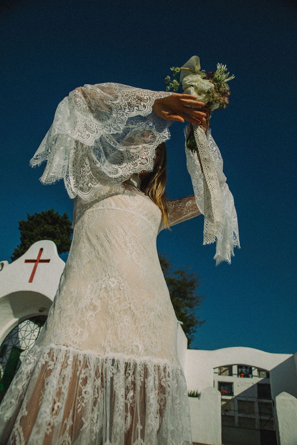 A vintage white lace wedding dress with delicate details displayed outdoors against a deep blue sky background.