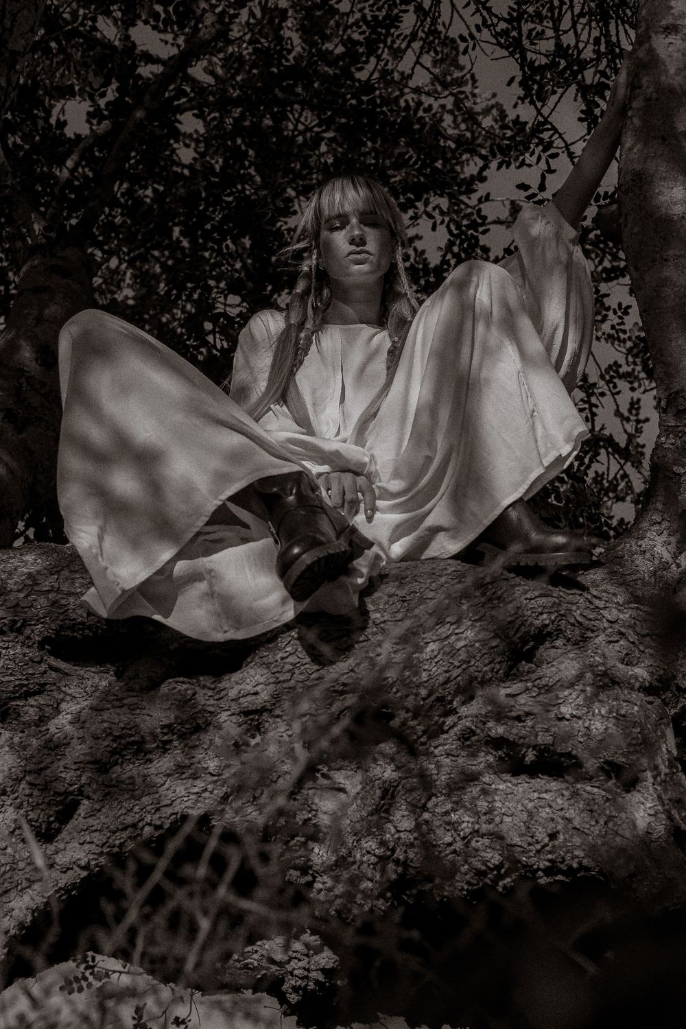 A black and white artistic photo series showing a figure in flowing white fabric reclining among tree branches.