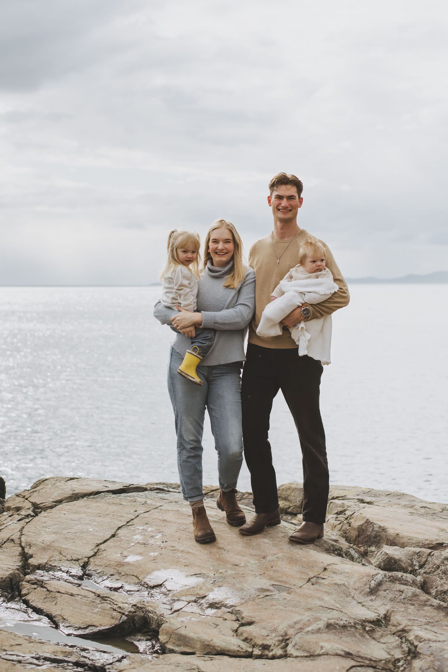A happy family shares joyful moments together on a rocky coastal shoreline with an overcast sky in the background.