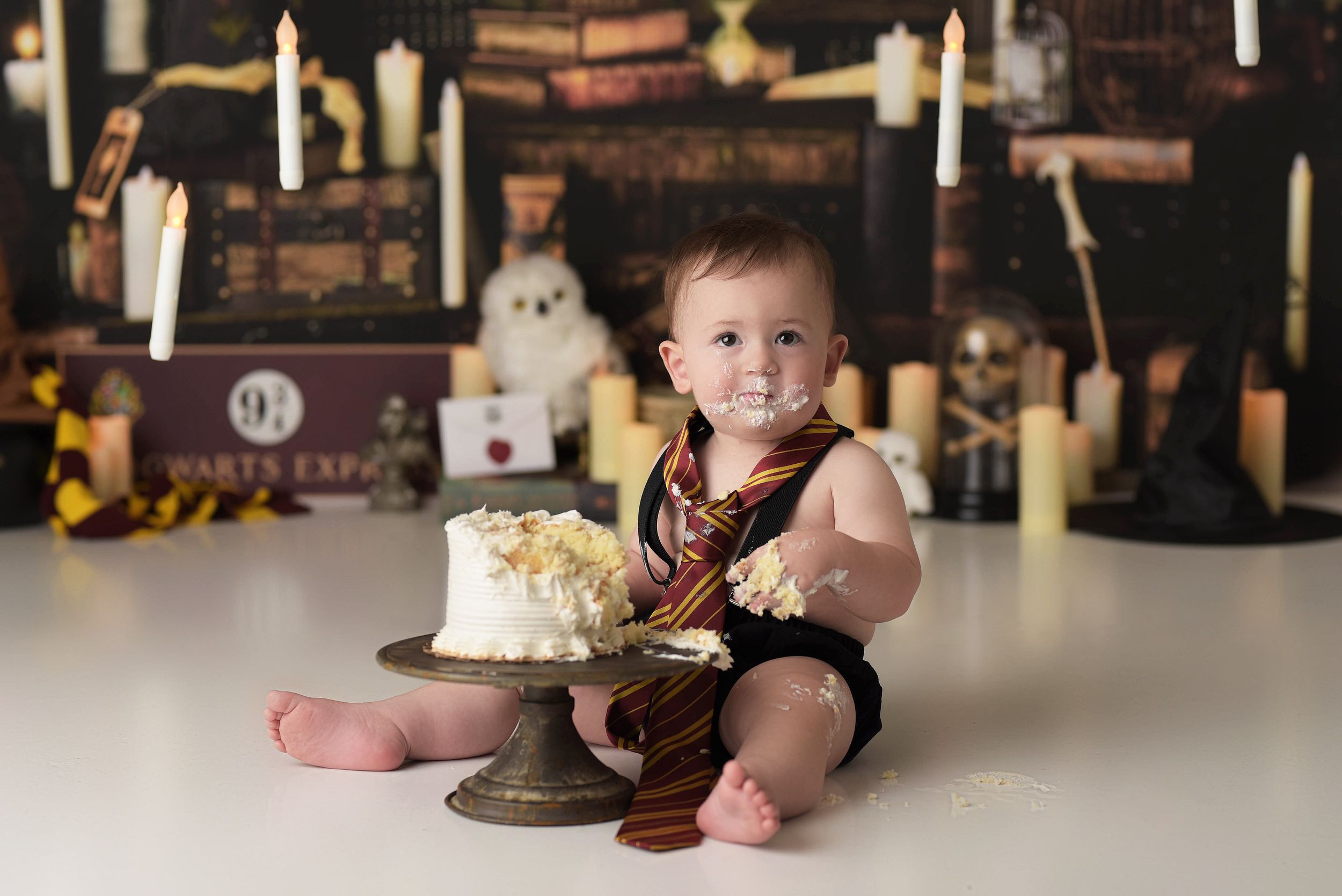 Baby boy dressed up as Harry Potter for his first birthday cake smash with a Hogwarts wizard backdrop