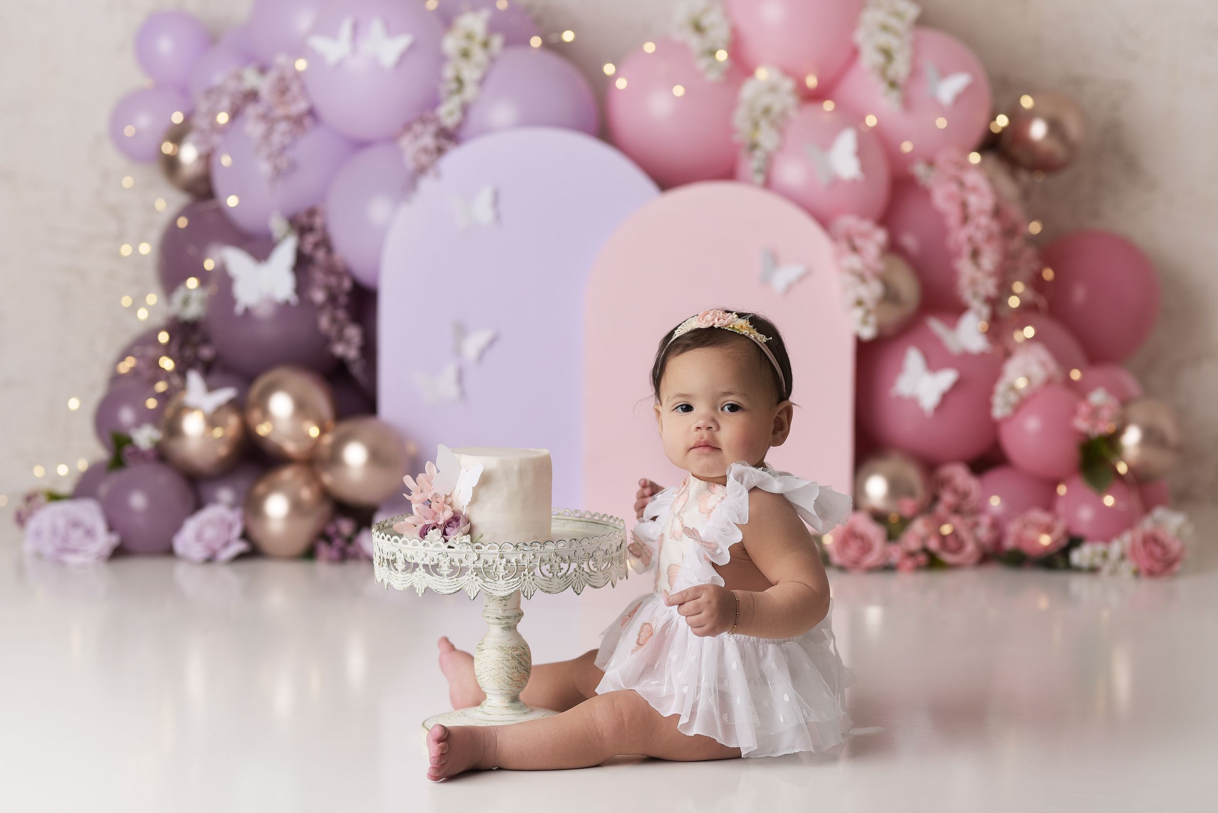 Baby girl with her birthday cake in front of a pink and purple balloon garland in Colorado Springs