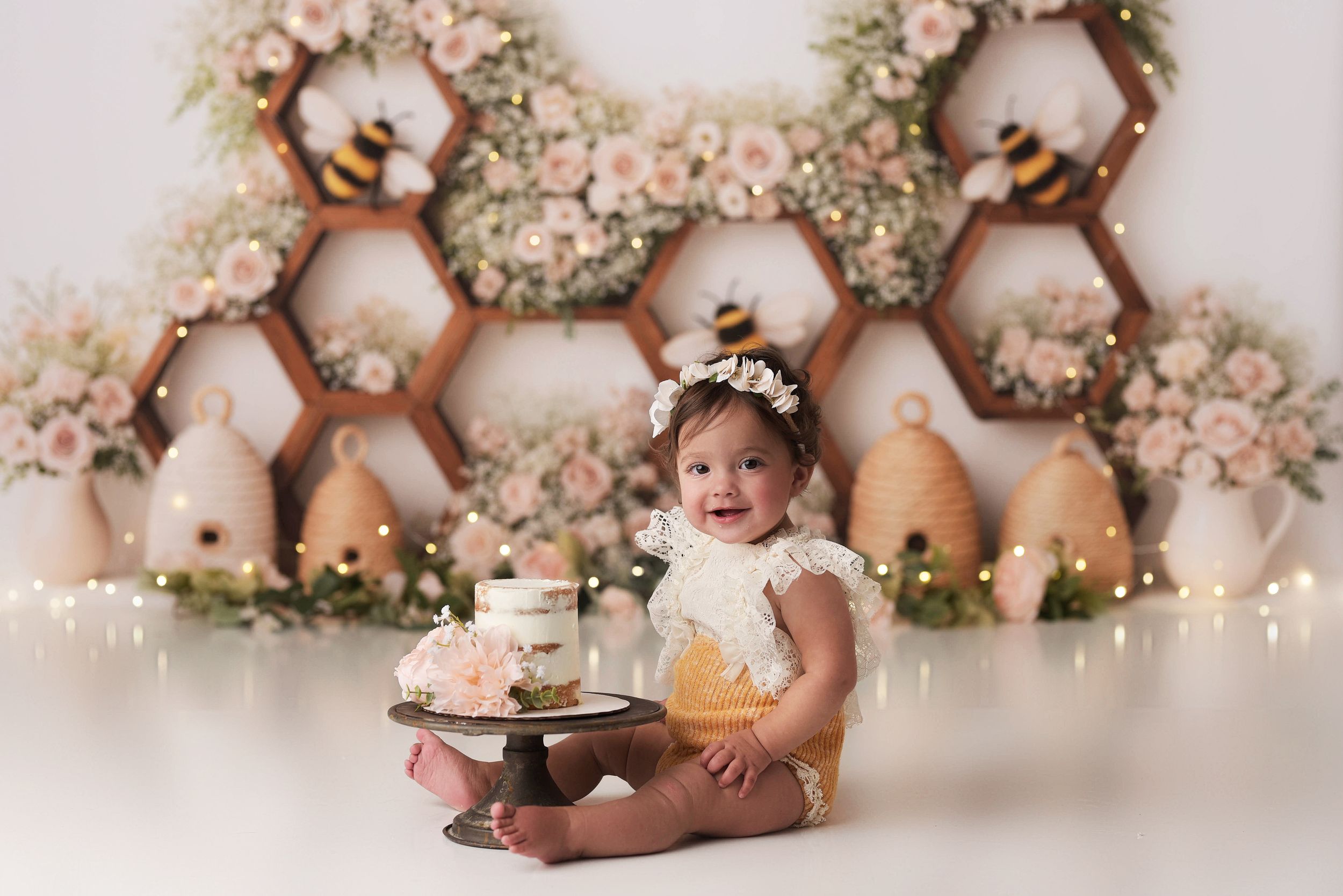 baby girl with her first birthday cake and a fun honeybee backdrop with lots of flowers