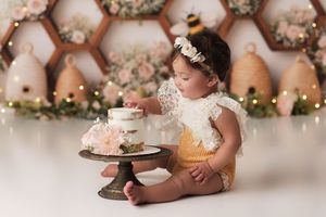 Baby girl in a yellow outfit with a rustic floral honeybee backdrop and a birthday cake