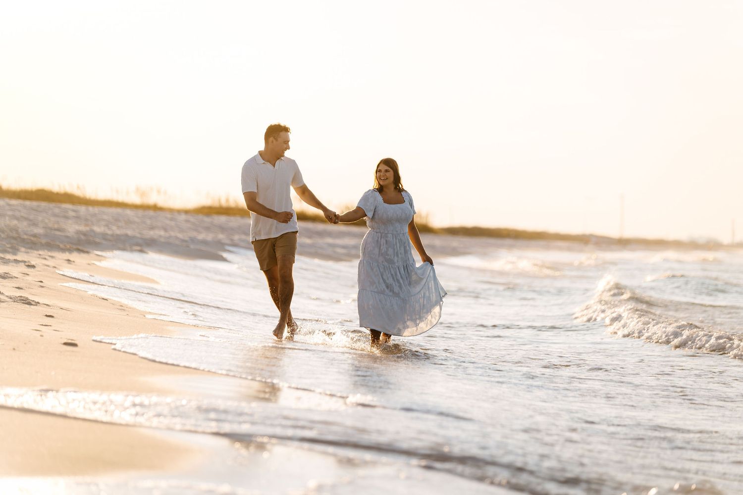 A couple holding hands while running along a sunset beach with waves gently rolling in. Fun couples activities in Fort Walton Beach Florida.