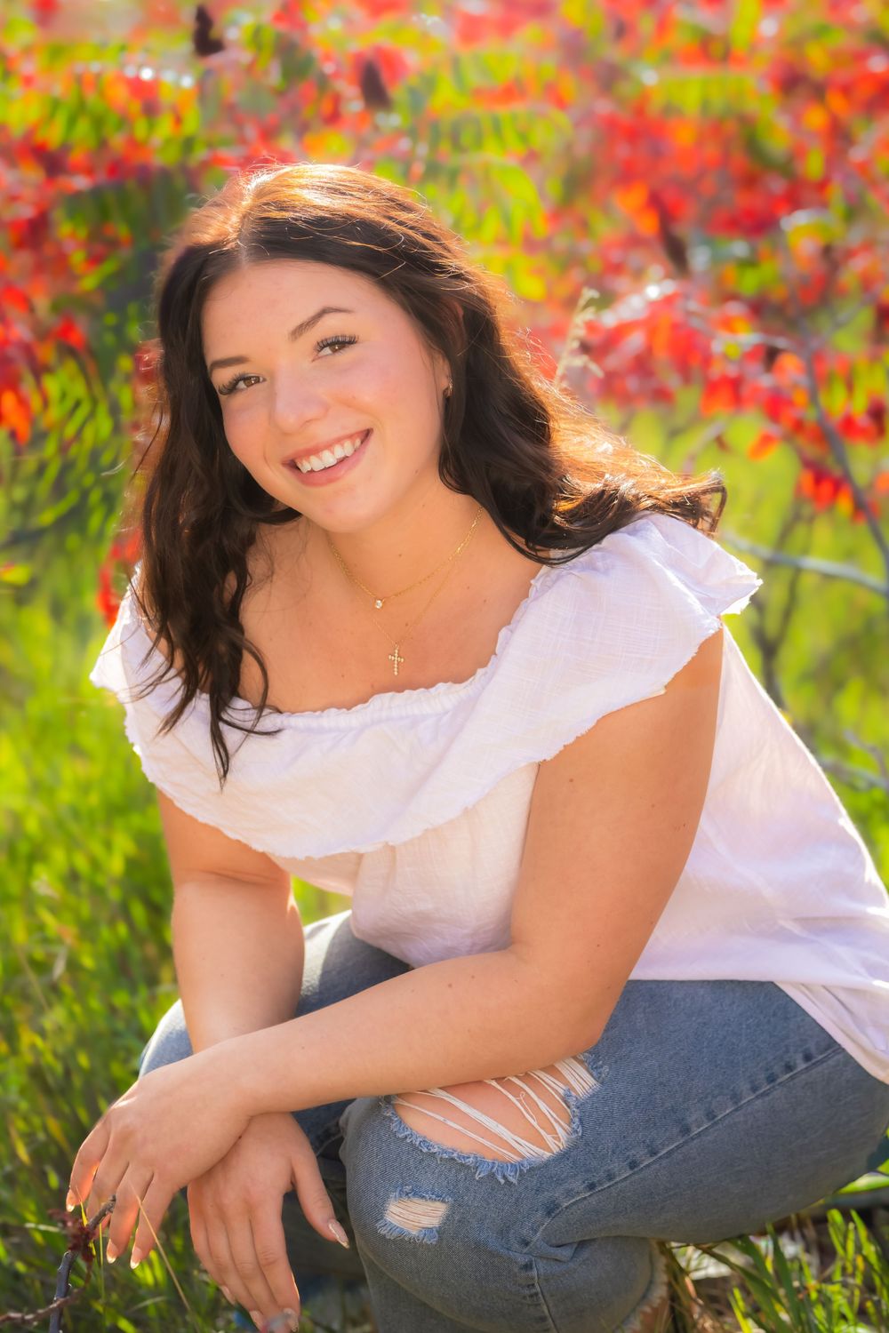 A portrait taken outdoors with vibrant red fall foliage in the background and soft natural lighting.