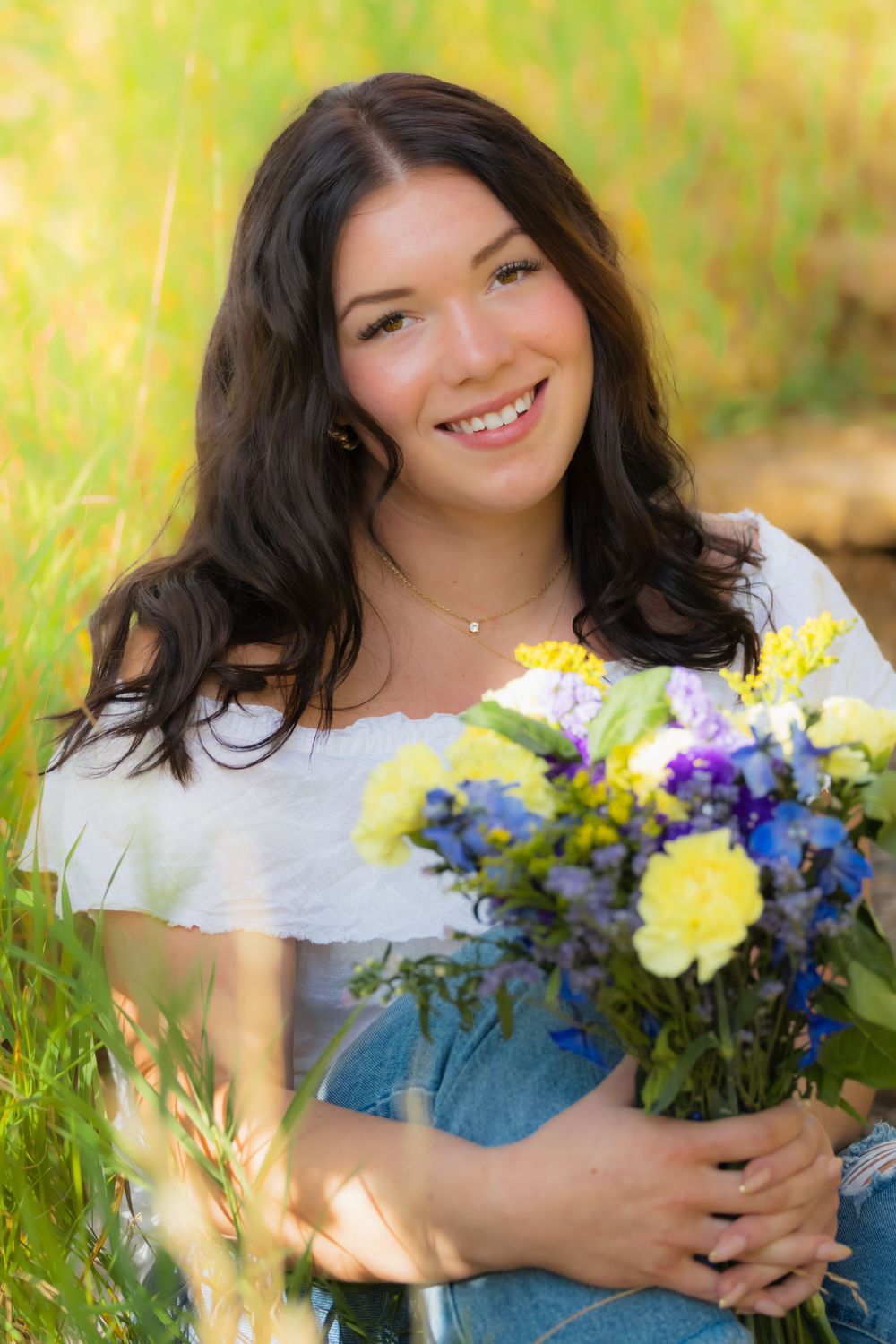 A joyful portrait in a field holding a vibrant bouquet of yellow, blue and purple flowers on a sunny day.