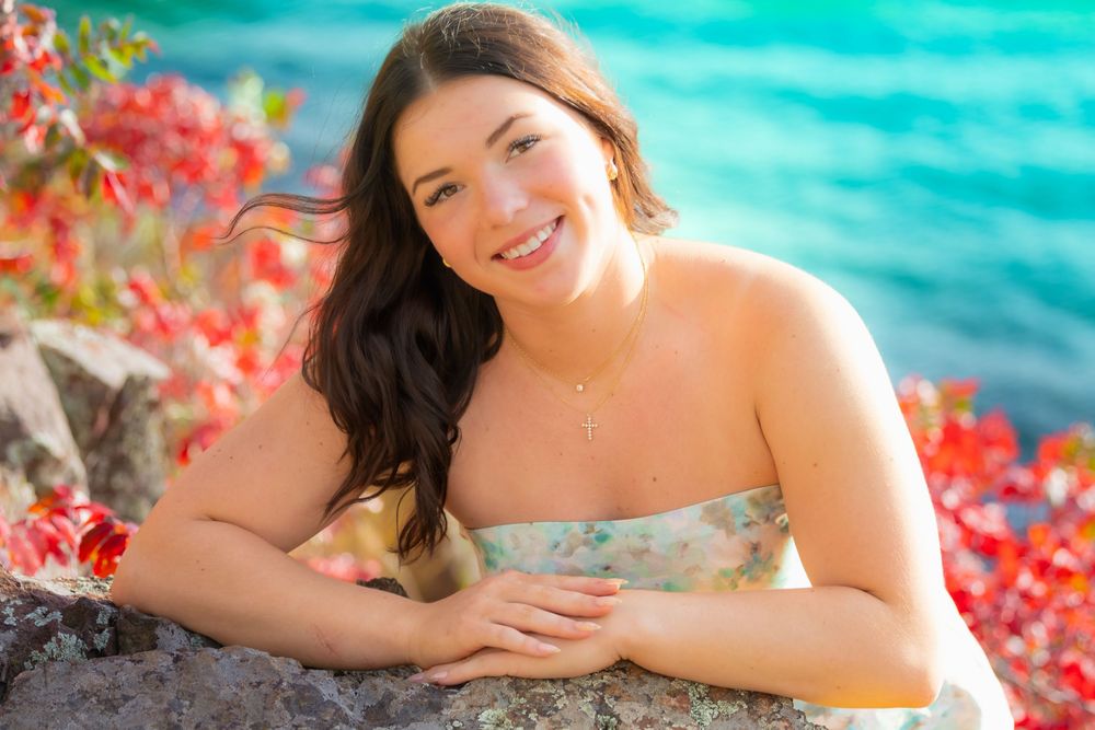 Woman in a tropical setting with turquoise water and vibrant red flowers in the background.