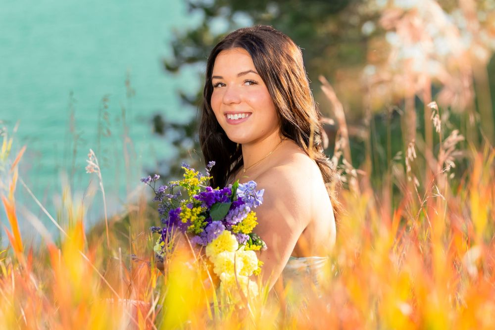 A person sits in a field of golden wildflowers and tall grass against a teal-colored background.