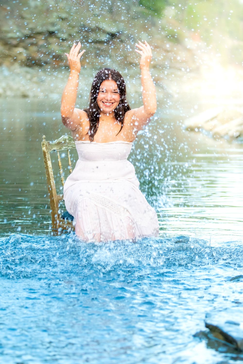A playful splash in a lake wearing a white dress while water droplets sparkle in the sunlight.
