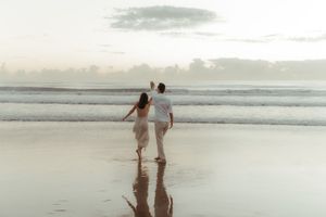 A couple walks hand in hand along a misty beach shoreline at sunset creating a romantic silhouette.