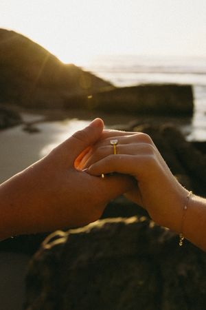 A romantic sequence of hands exchanging an engagement ring at sunset against a mountainous backdrop.