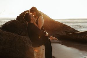 A couple shares an intimate moment on coastal rocks during golden hour at the beach.