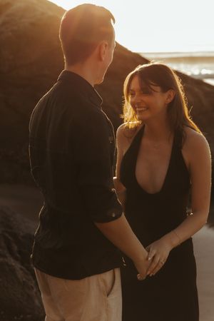 A couple shares a joyful moment together during golden hour on a beach, both wearing black outfits.