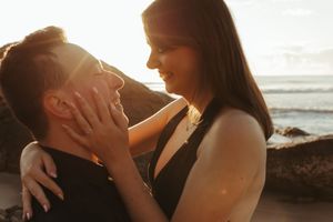 Intimate couple portrait session at beach during golden hour with sun flare.