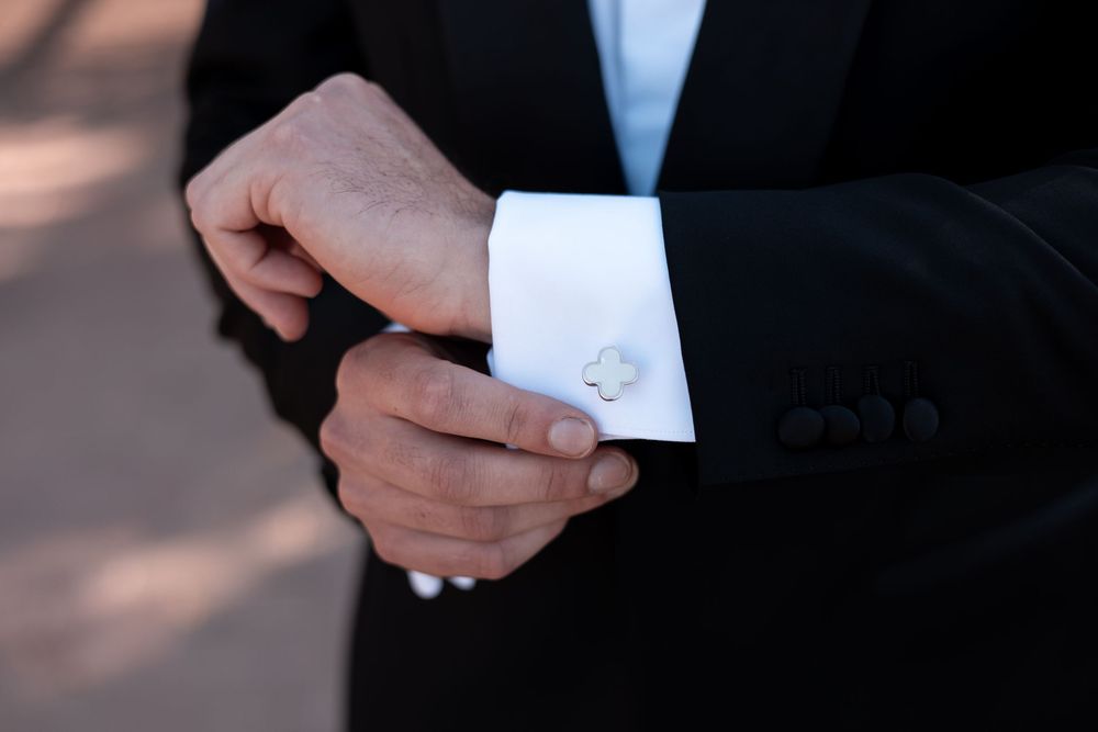 Close-up view of hands adjusting white shirt cuffs and cufflinks in a formal setting.