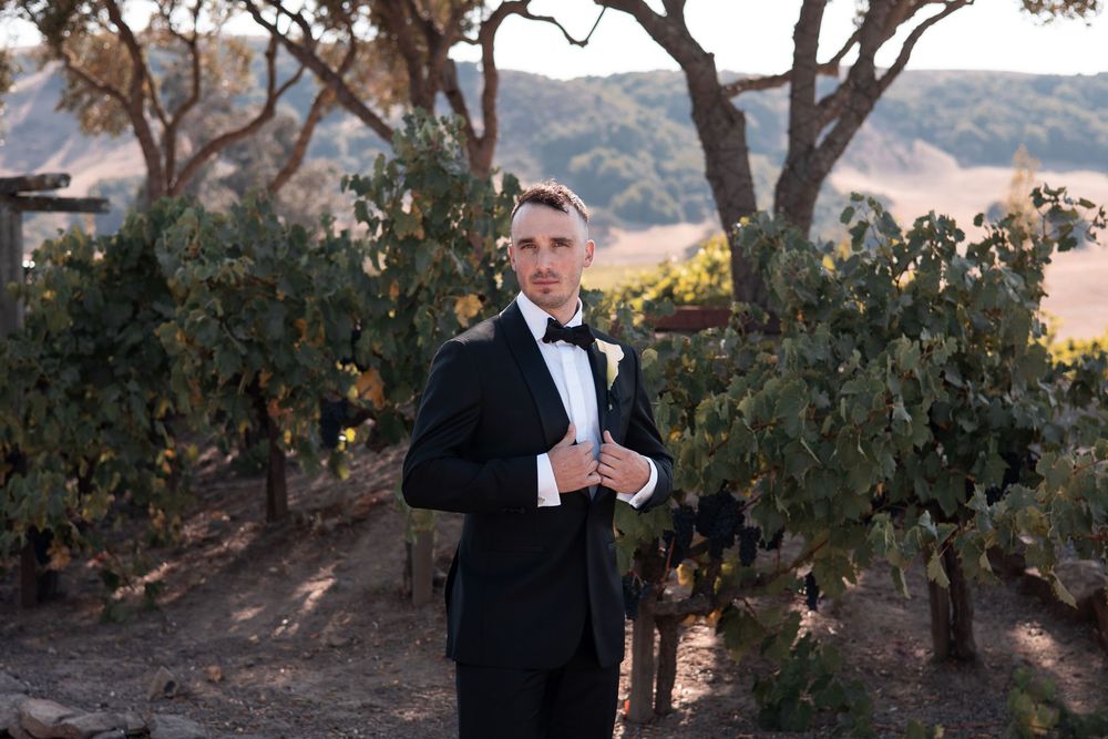 Wedding couple shares a romantic moment under oak trees at sunset in a scenic outdoor setting.