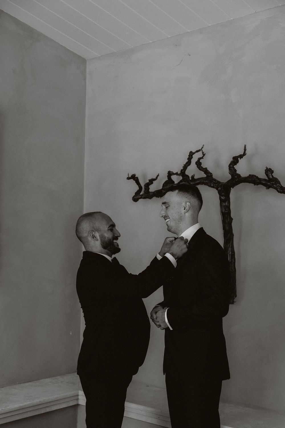 A series of black and white photos showing two people in dark clothing interacting against a white wall.