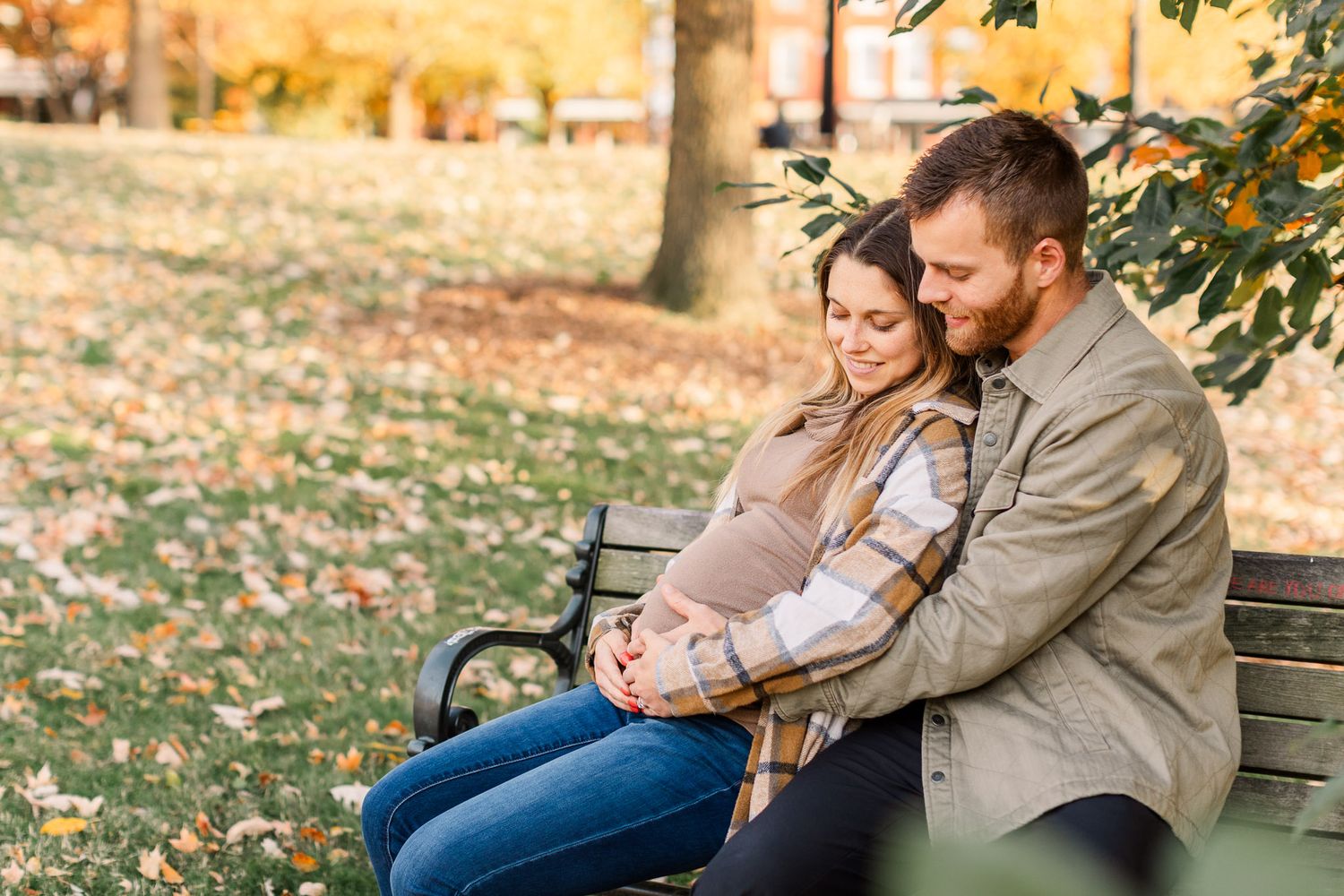 Pregnant wife with husband sitting on a bench smiling at her baby bump at Libby Hill Park in Richmond Va