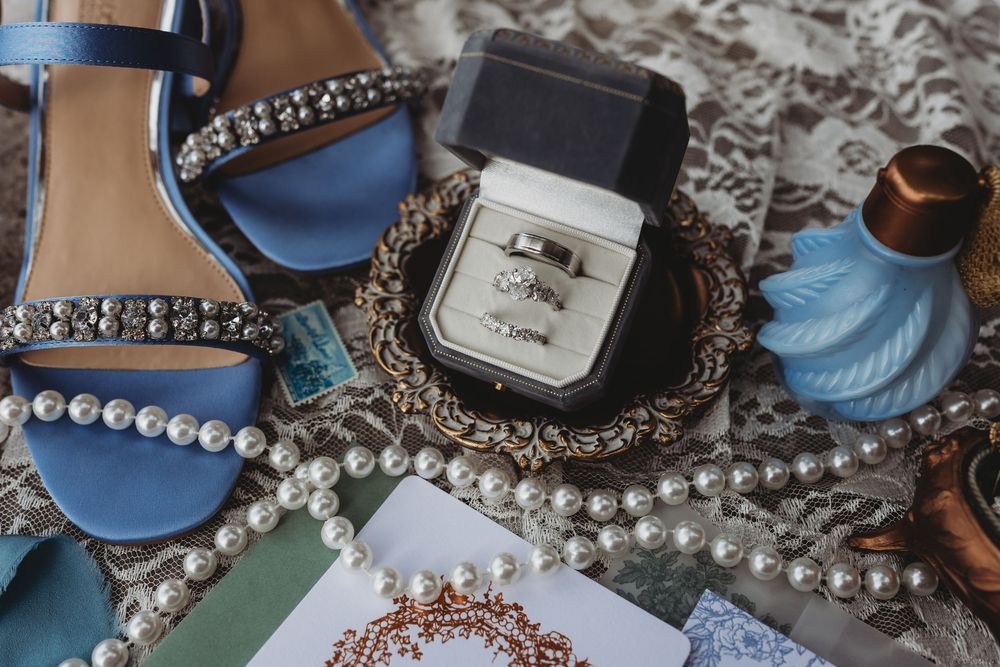 Elegant wedding details including pearl necklaces, perfume bottles, and vintage accessories arranged on a reflective surface.