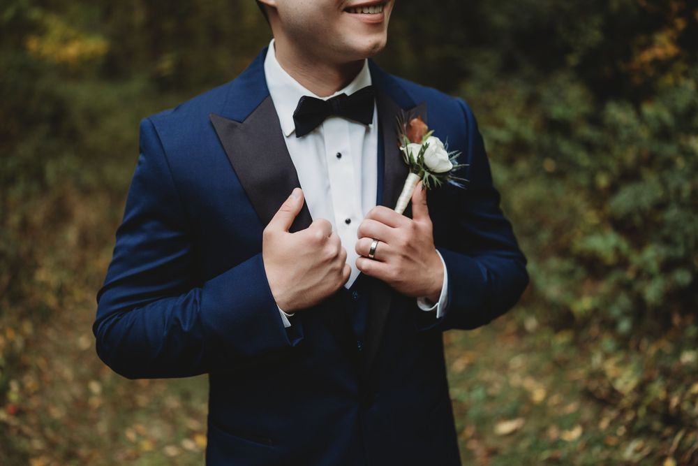 A groom in a classic black tuxedo and bow tie adjusts his collar during wedding preparations.