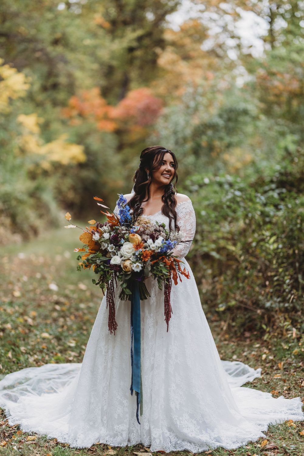 Two brides in white lace wedding dresses hold autumn bouquets with orange and blue flowers in a garden setting.