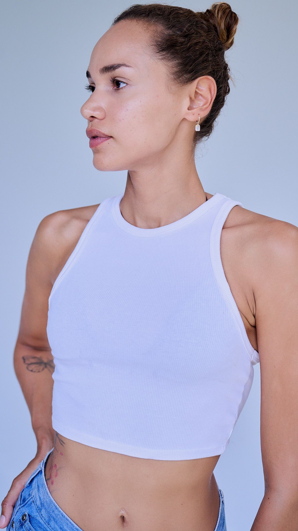 Model poses in white crop top and denim against light blue background in series of artistic fashion shots.