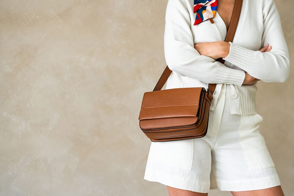 Woman in white blazer outfit modeling different angles with brown leather shoulder bag against neutral wall.