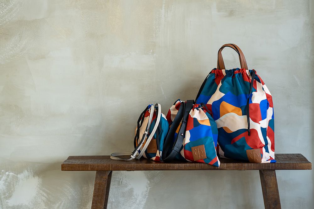 Person in denim overalls and colorful bag rests on wooden bench with artistic composition.