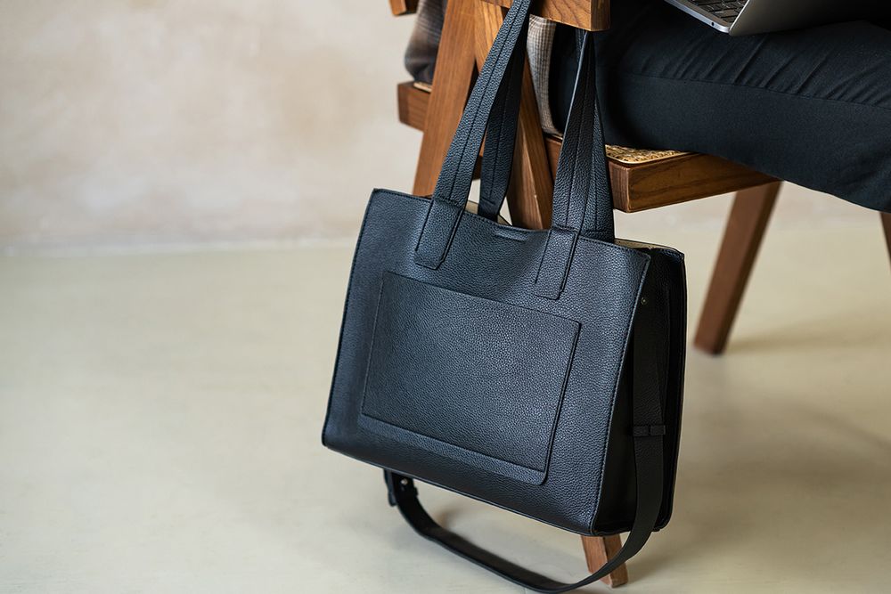 A black leather tote bag with structured sides and top handles shown from multiple angles on a light background.