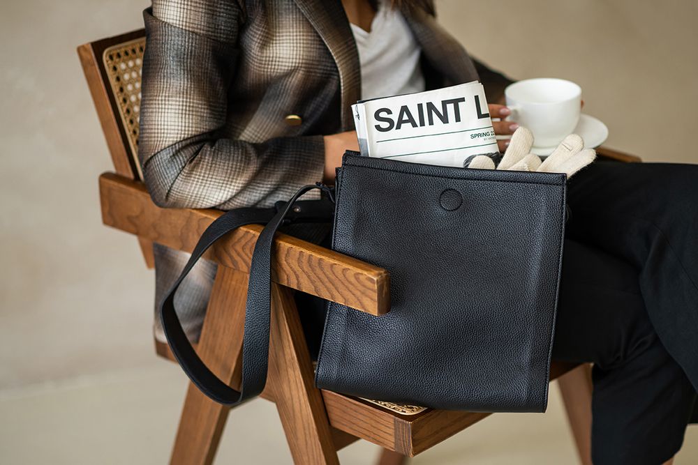 A wooden chair with a black leather handbag placed on its seat in a neutral-toned interior setting.