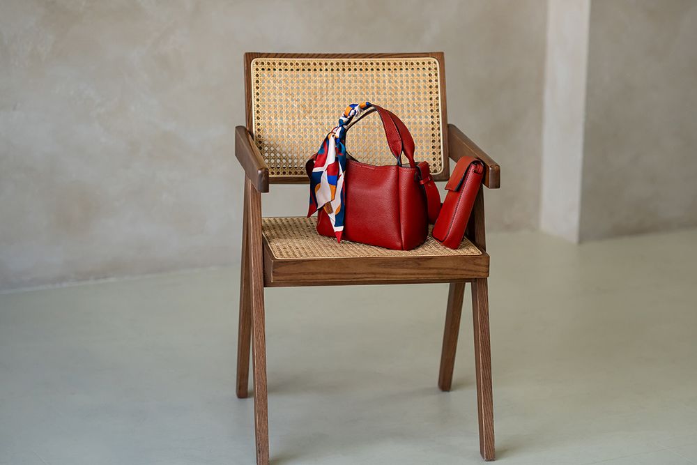 Red leather handbag displayed on wooden chair against neutral wall in minimalist product photography setup.
