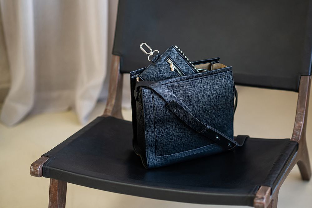 Black leather handbag with silver hardware displayed on wooden surface in retail setting.