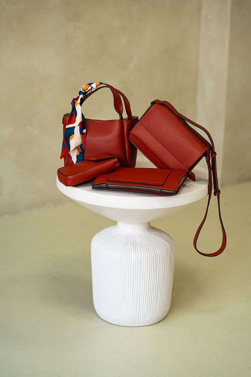 Red leather crossbody bag displayed on white pedestal against beige background in multiple angles.