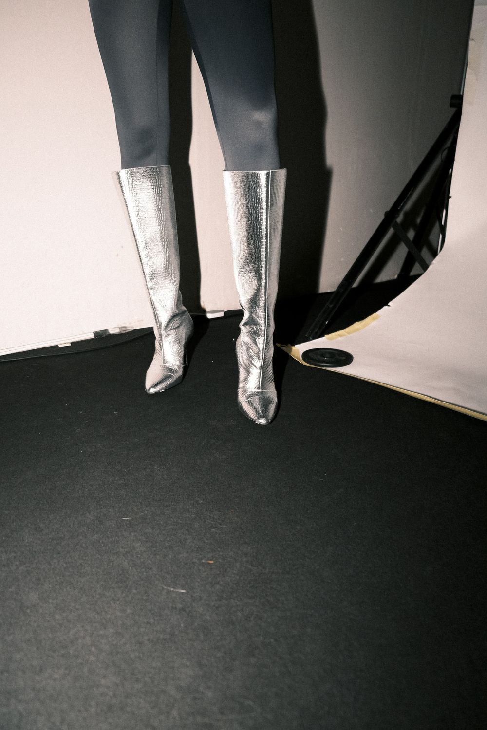 A pair of metallic silver knee-high boots against a dark background with dramatic lighting.