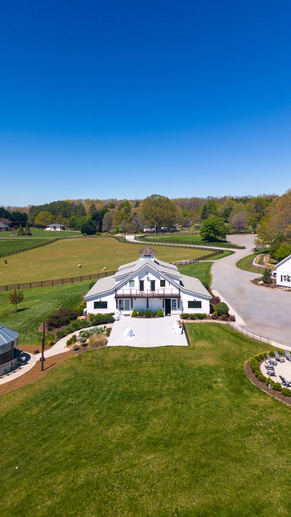 Aerial view of a white farmhouse venue with manicured lawns and winding driveway.