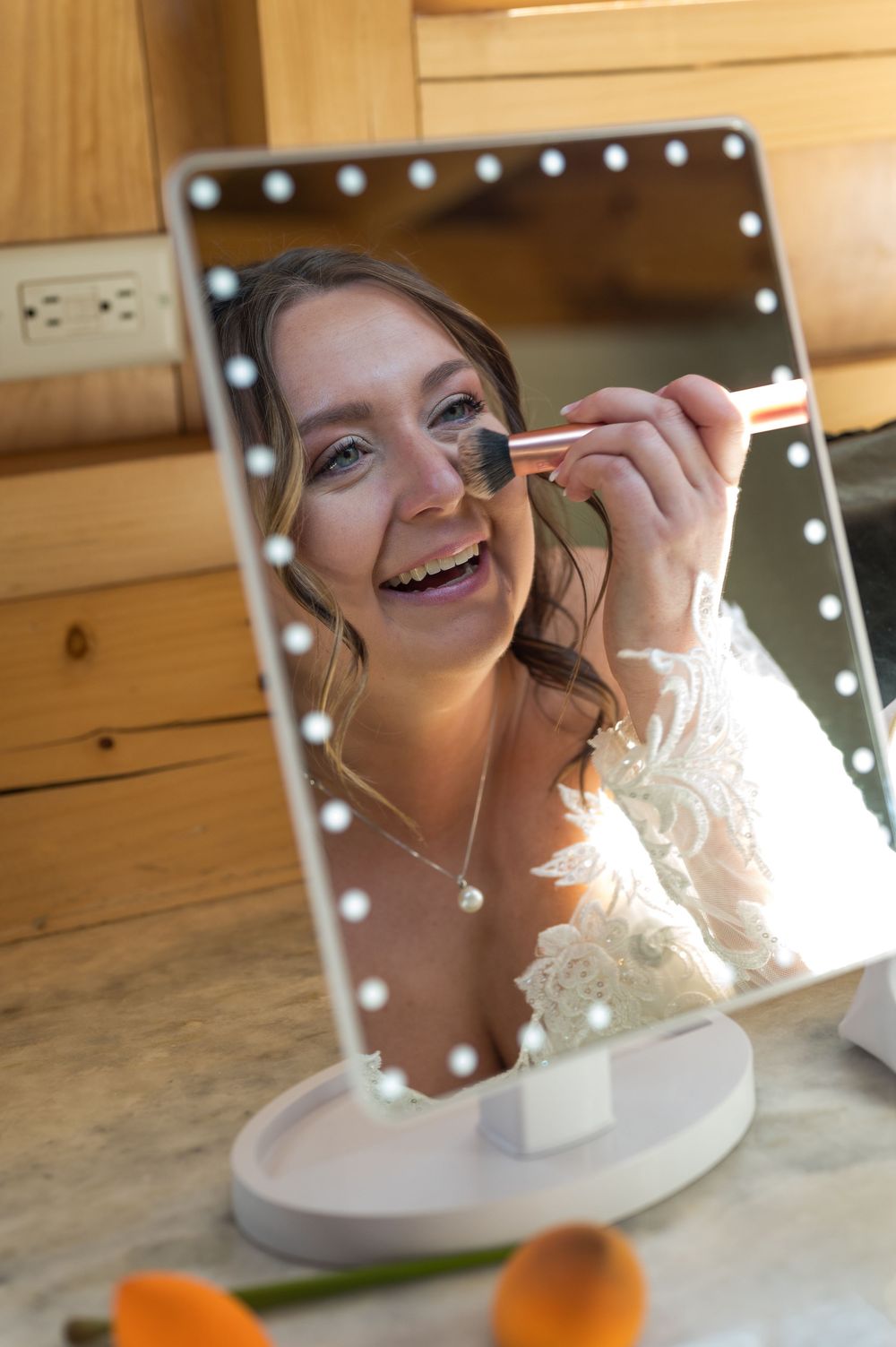 Getting ready shots in a mirror with makeup being applied before a wedding ceremony.