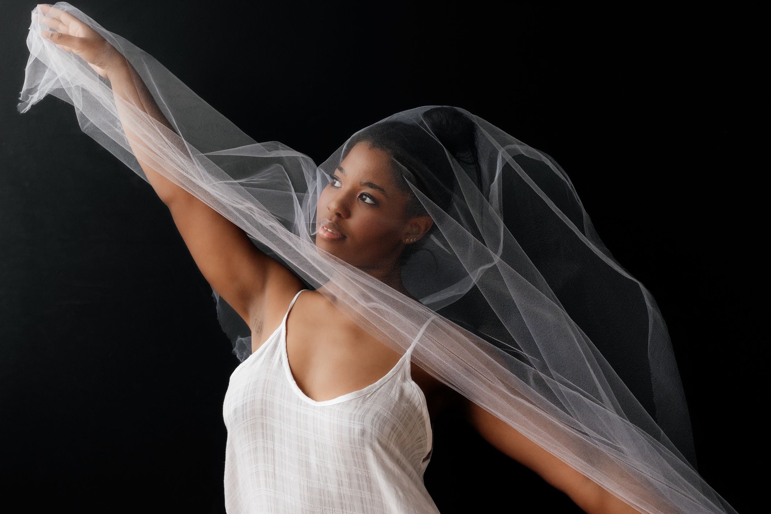 A dancer in white moves gracefully with flowing sheer fabric creating an ethereal effect against a dark background.