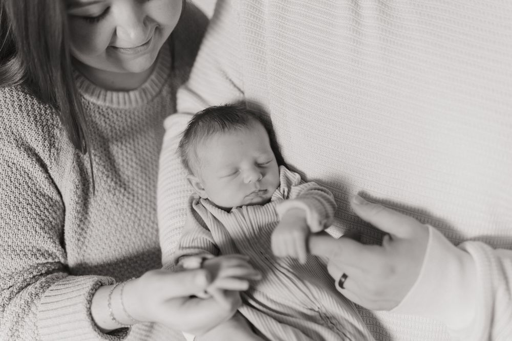 Mother holding and comforting newborn baby in cozy white setting.