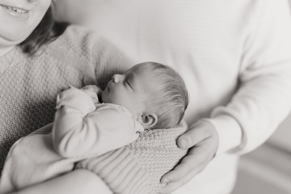 A series of black and white images showing tender moments between parent and newborn baby in soft light.