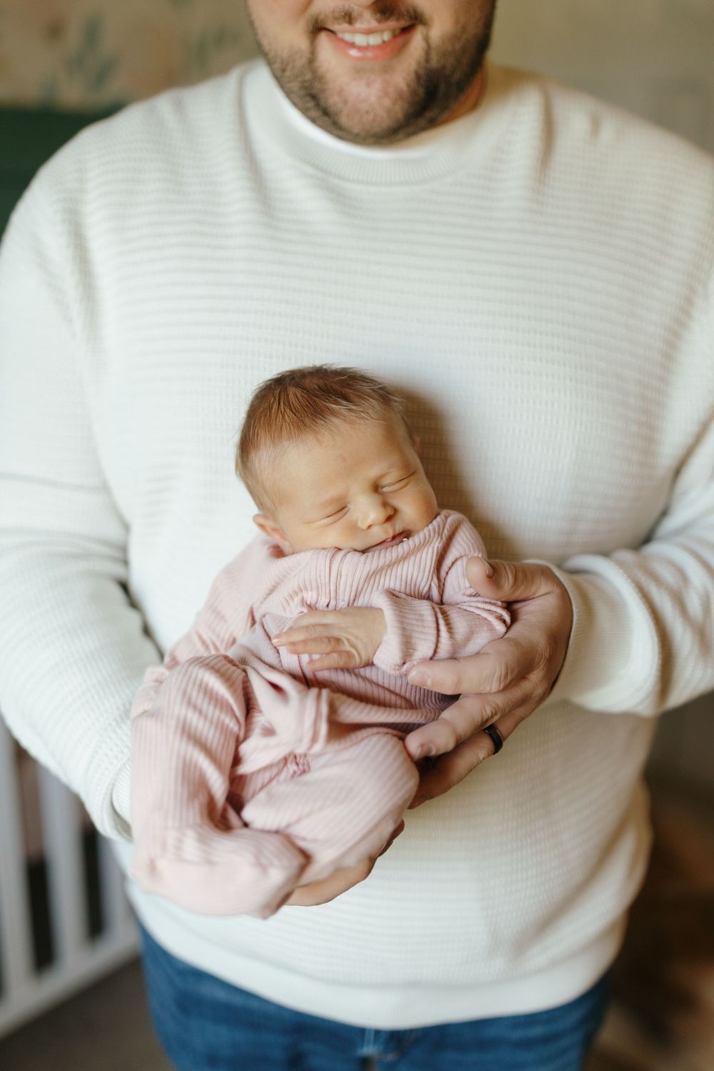 A parent in a white sweater holds a sleeping newborn baby wearing a soft pink outfit.