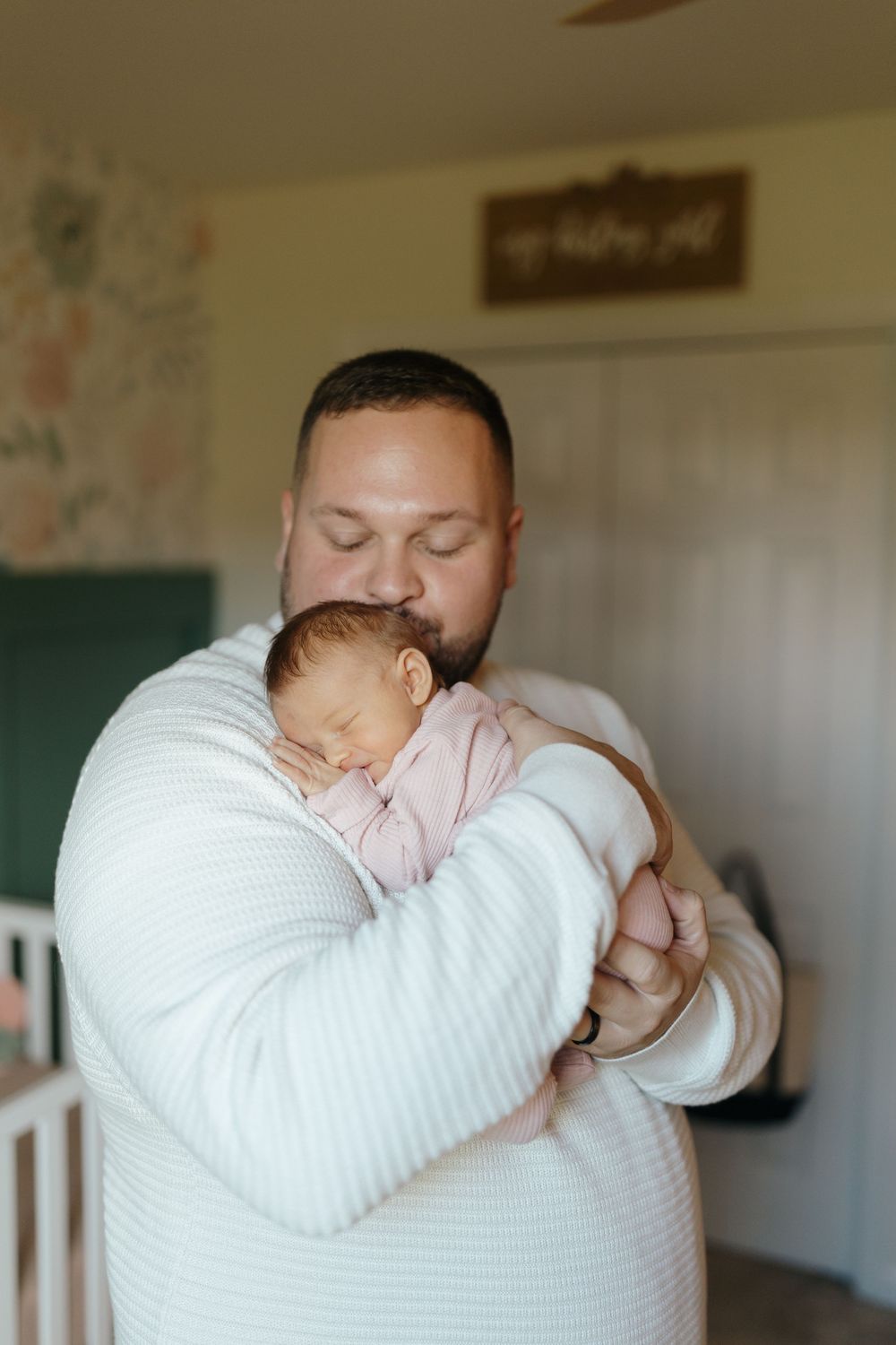 A tender moment showing a parent in white cradling and kissing a sleeping baby in pink.