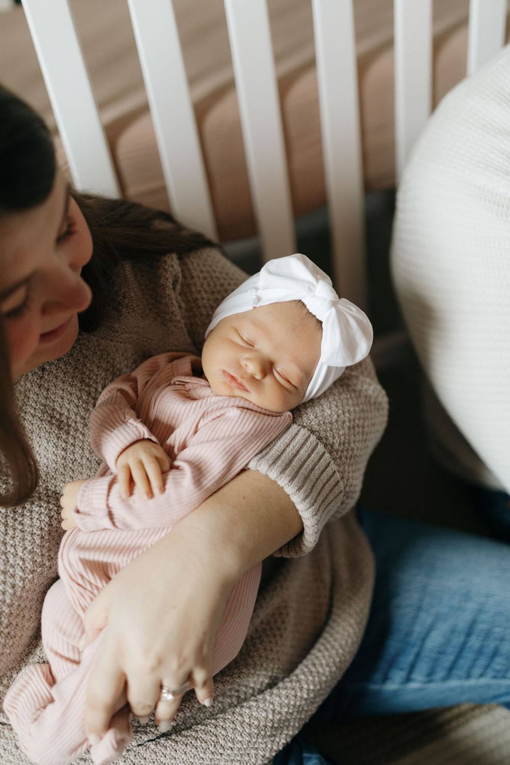 Sleeping newborn baby wearing pink knit sweater rests peacefully on textured gray blanket.