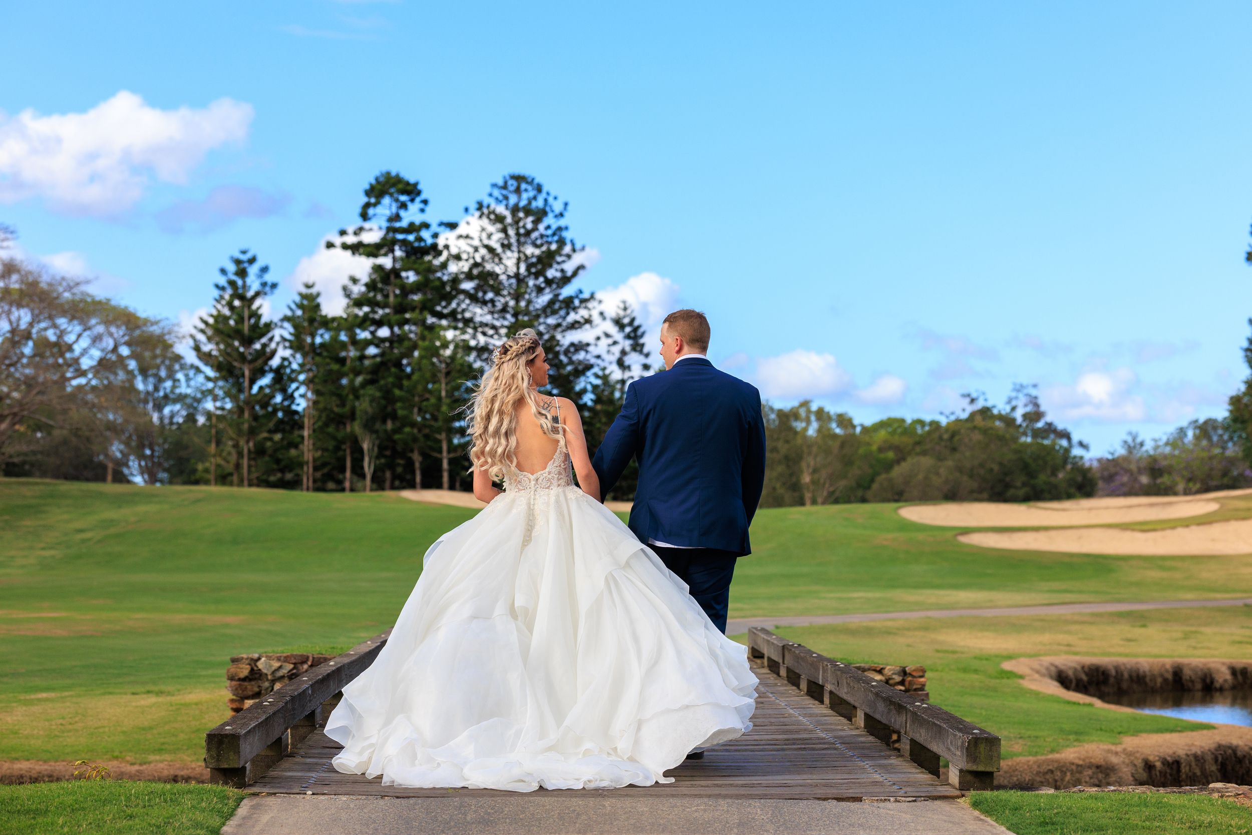 A couple in wedding attire stands on a wooden walkway overlooking  Brisbane golf course.