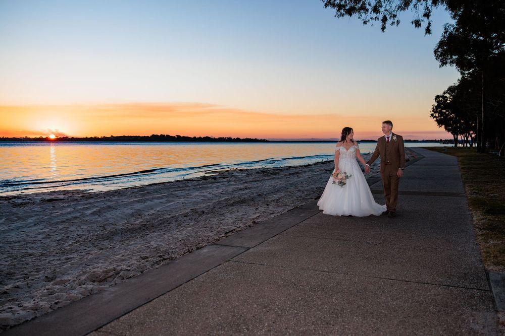 Bride and groom walk along waterfront path at sunset wedding photography