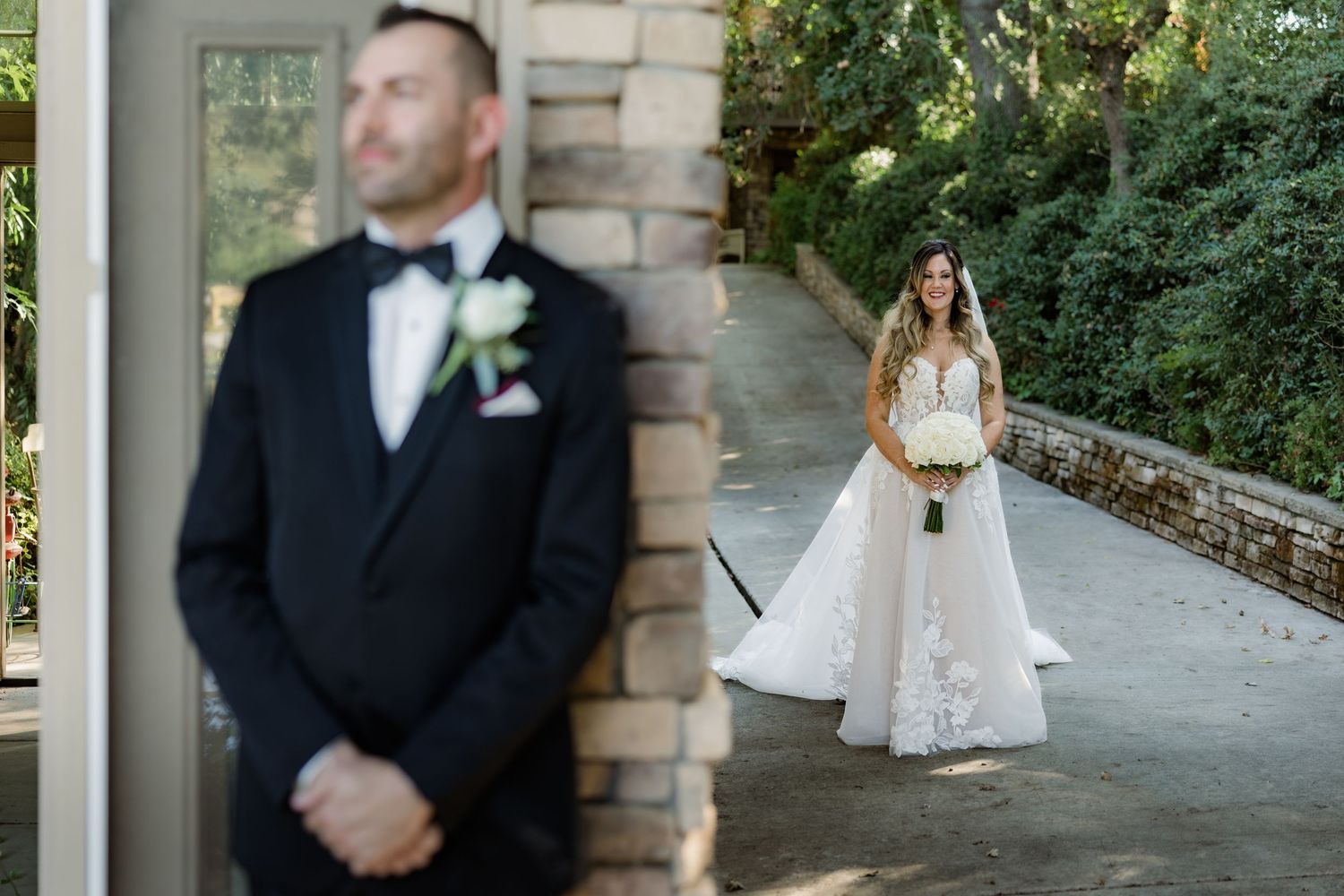 Elegant wedding party portraits taken against a stone brick wall with greenery in an outdoor setting.