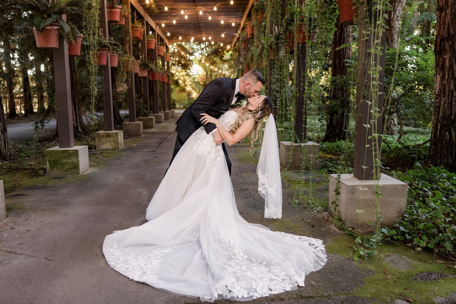 A romantic wedding moment captured on a string-lit pathway surrounded by lush greenery.